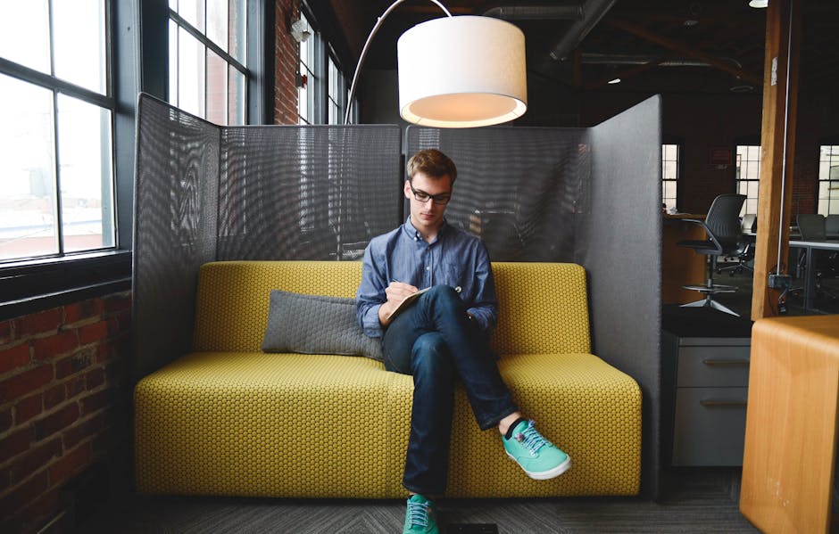 Young man writing on a notebook while sitting on a couch in a modern coworking space.